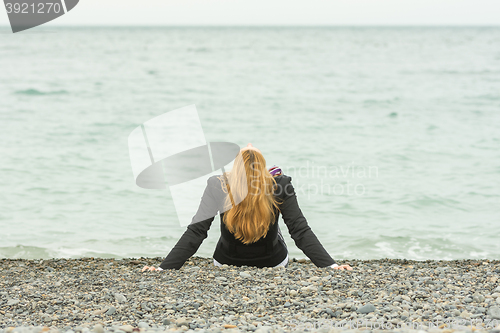 Image of She sits back on a pebble beach by the sea on a cloudy day, his head thrown back