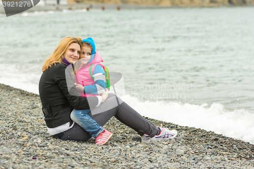 Image of Mom and daughter in the arms sit on the beach on a cool day and watching the surf