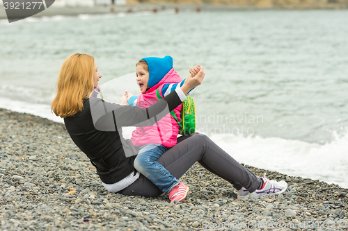 Image of Mom and daughter having fun playing while sitting on the beach on a cool day