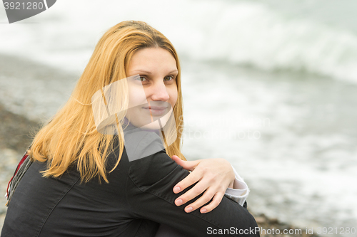 Image of Portrait of sitting on the beach mysteriously smiling girl in cloudy weather