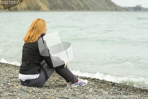 Image of Girl in a cool day sitting on the beach and looking thoughtfully into the distance