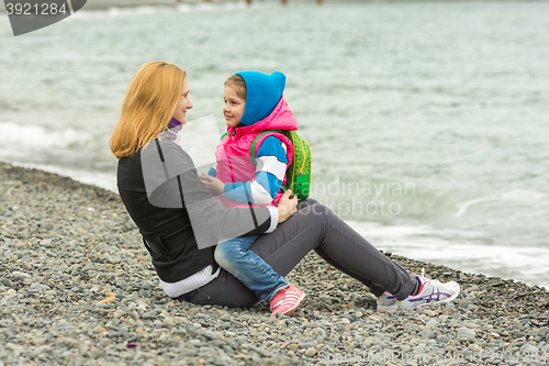 Image of Mother and daughter tenderly looking at each other sitting on the beach on a cool day