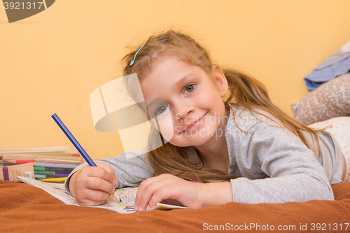 Image of Cheerful little girl draws lying on his stomach with a pencil on paper