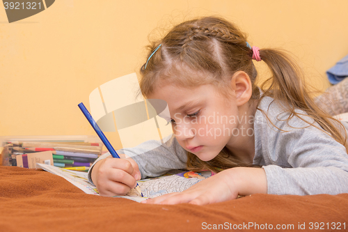 Image of Little girl draws a hard lying on his stomach with a pencil on paper