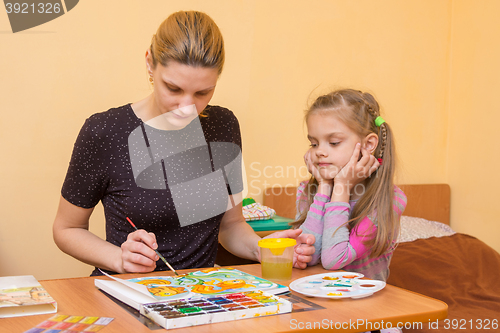 Image of A little girl is watching carefully for a teacher who shows how to paint watercolor