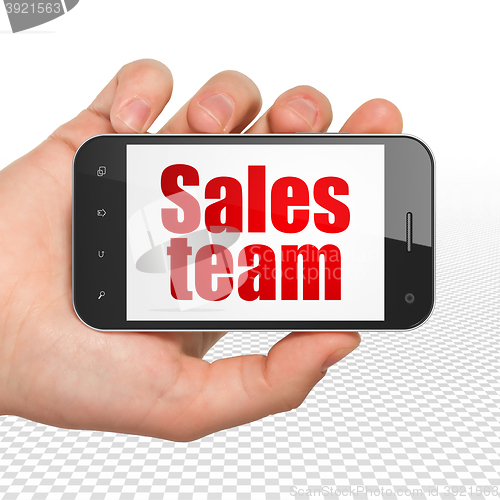 Image of Advertising concept: Hand Holding Smartphone with Sales Team on display