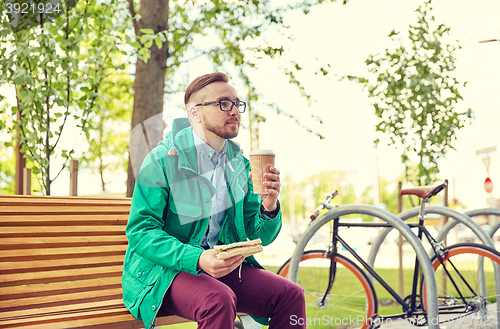 Image of happy young hipster man with coffee and sandwich