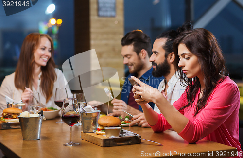 Image of woman with smartphone and friends at restaurant