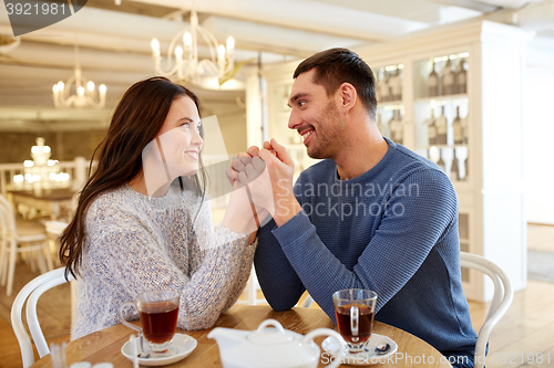 Image of happy couple with tea holding hands at restaurant