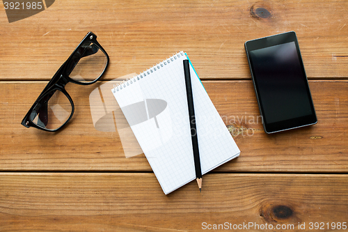 Image of close up of notepad, smartphone and eyeglasses