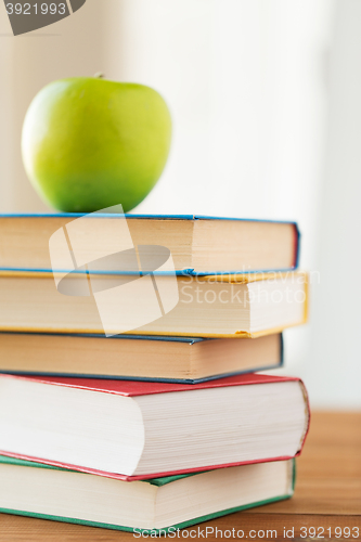 Image of close up of books and green apple on wooden table