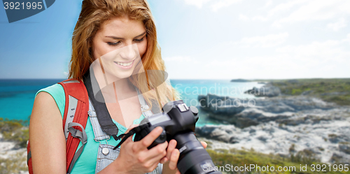 Image of happy woman with backpack and camera over seashore