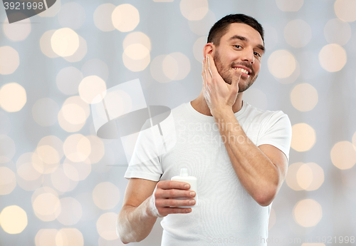 Image of happy young man applying cream or lotion to face