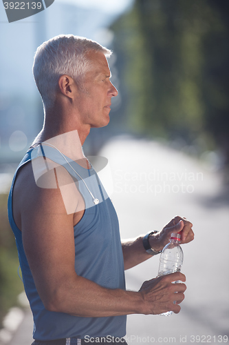 Image of senior jogging man drinking fresh water from bottle