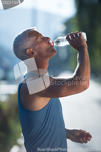 Image of senior jogging man drinking fresh water from bottle