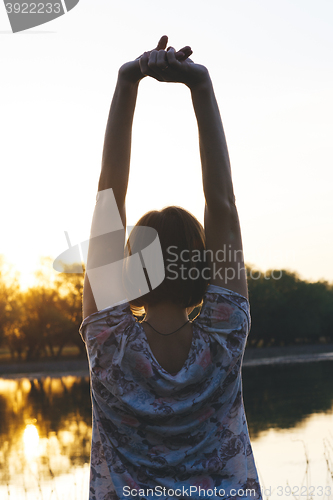 Image of the girl raised her arms up at sunset