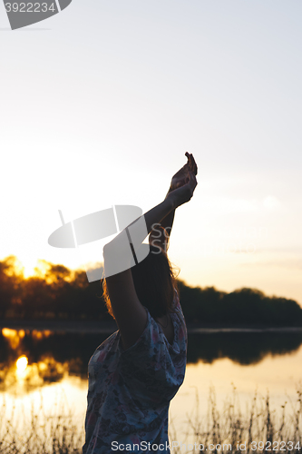 Image of the girl raised her arms up at sunset