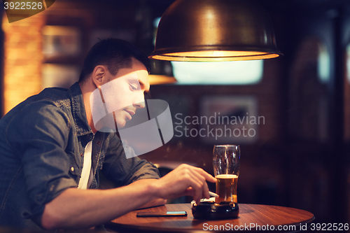 Image of man drinking beer and smoking cigarette at bar