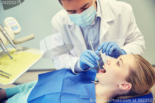 Image of male dentist in mask checking female patient teeth