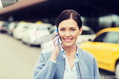 Image of smiling woman with smartphone over taxi in city