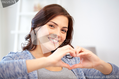 Image of happy young woman showing heart with hands at home