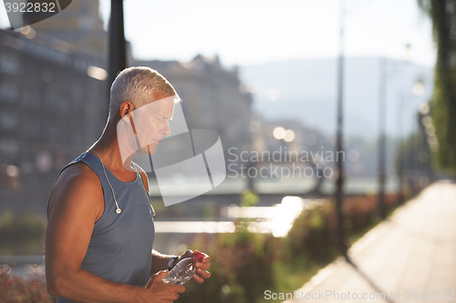 Image of senior jogging man drinking fresh water from bottle