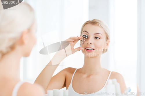 Image of woman with curler curling eyelashes at bathroom