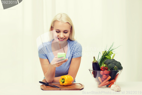 Image of smiling woman with smartphone cooking vegetables