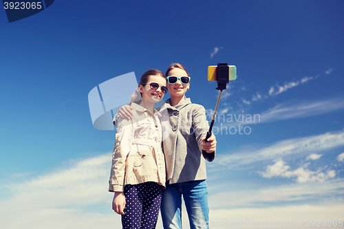 Image of happy girls with smartphone selfie stick