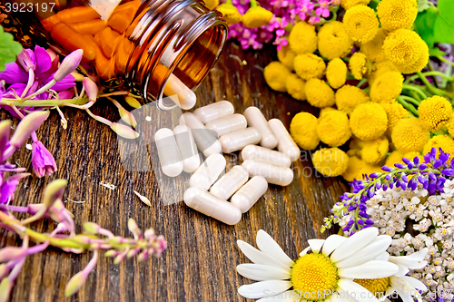 Image of Capsules in brown jar with flowers on dark board