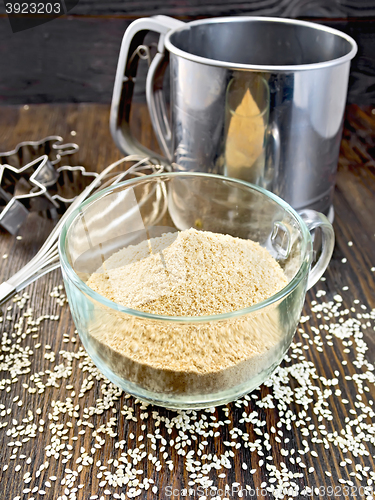 Image of Flour sesame in cup with sieve on dark board