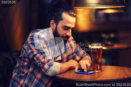 Image of man with smartphone and beer texting at bar