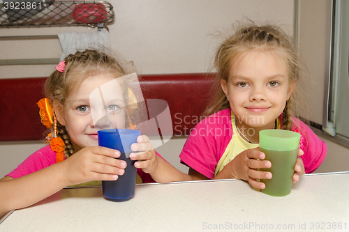 Image of Two girls sisters on the train sitting at the table on the lower place in the second-class compartment wagon with glasses in hand