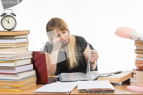 Image of Student sadly looking at turning the pages in a folder at the desk among the stacks of books