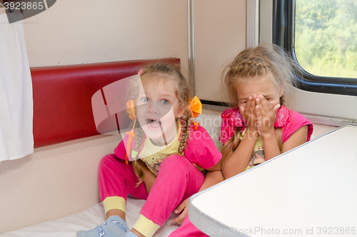 Image of Two cheerful little girls are sitting on the train on the lower second-class place car in the same pajamas