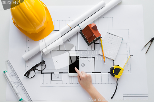 Image of close up of hand with blueprint and smartphone