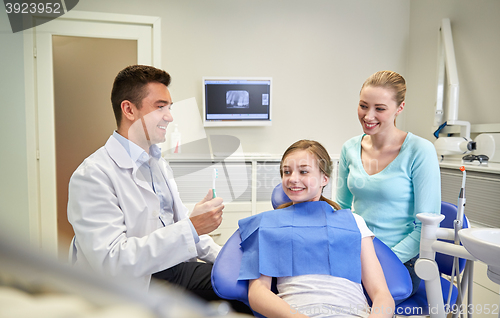 Image of happy dentist showing toothbrush to patient girl