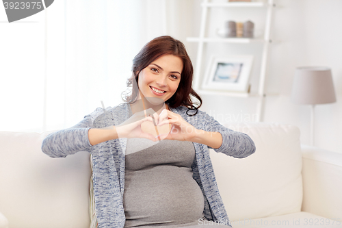 Image of happy pregnant woman making heart gesture at home