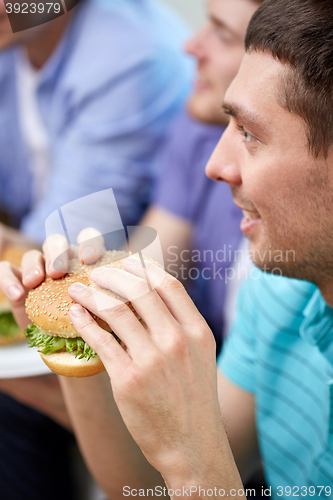 Image of close up of friends eating hamburgers at home