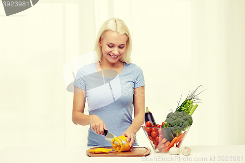 Image of smiling young woman chopping vegetables at home