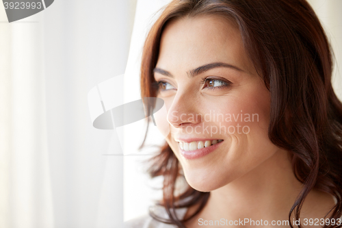 Image of happy young woman looking through window at home