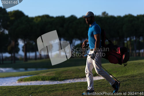 Image of golfer  walking and carrying golf  bag at beautiful sunset