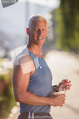 Image of senior jogging man drinking fresh water from bottle