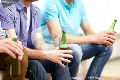 Image of happy male friends drinking beer at home