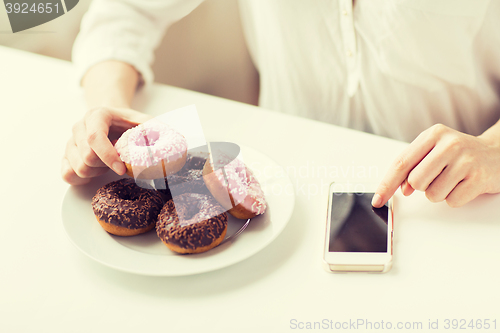 Image of close up of hands with smart phone and donuts