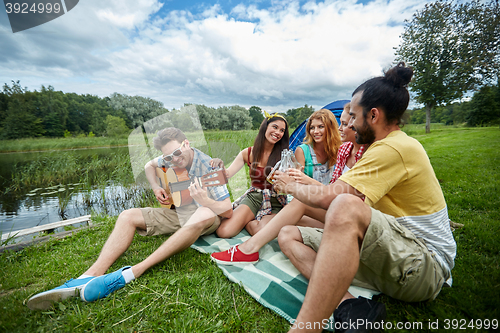 Image of happy friends with drinks and guitar at camping