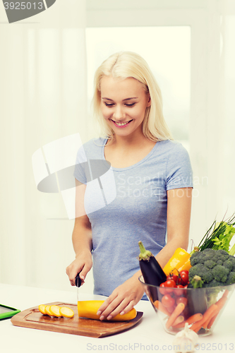 Image of smiling young woman chopping vegetables at home