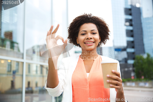 Image of happy woman with coffee showing ok up in city