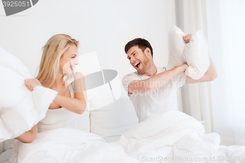 Image of happy couple having pillow fight in bed at home