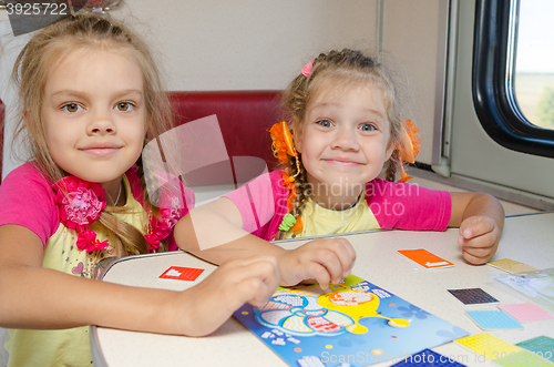 Image of Two little sisters in the train of fun playing at the table at the lower place in the second-class compartment wagon